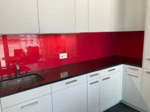 Crédence en verre laqué rouge brillant installée dans une cuisine moderne avec meubles blancs et plan de travail noir.