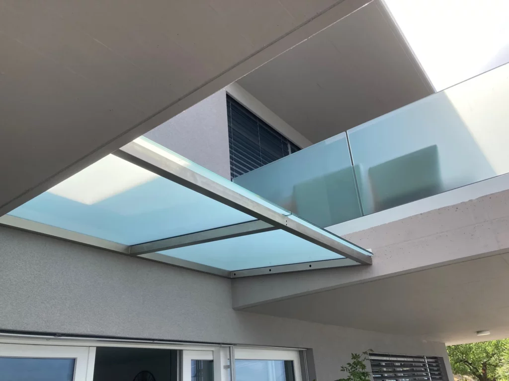 Marquise en verre opalin sur mesure avec structure métallique installée au-dessus d’une entrée d’habitation moderne.