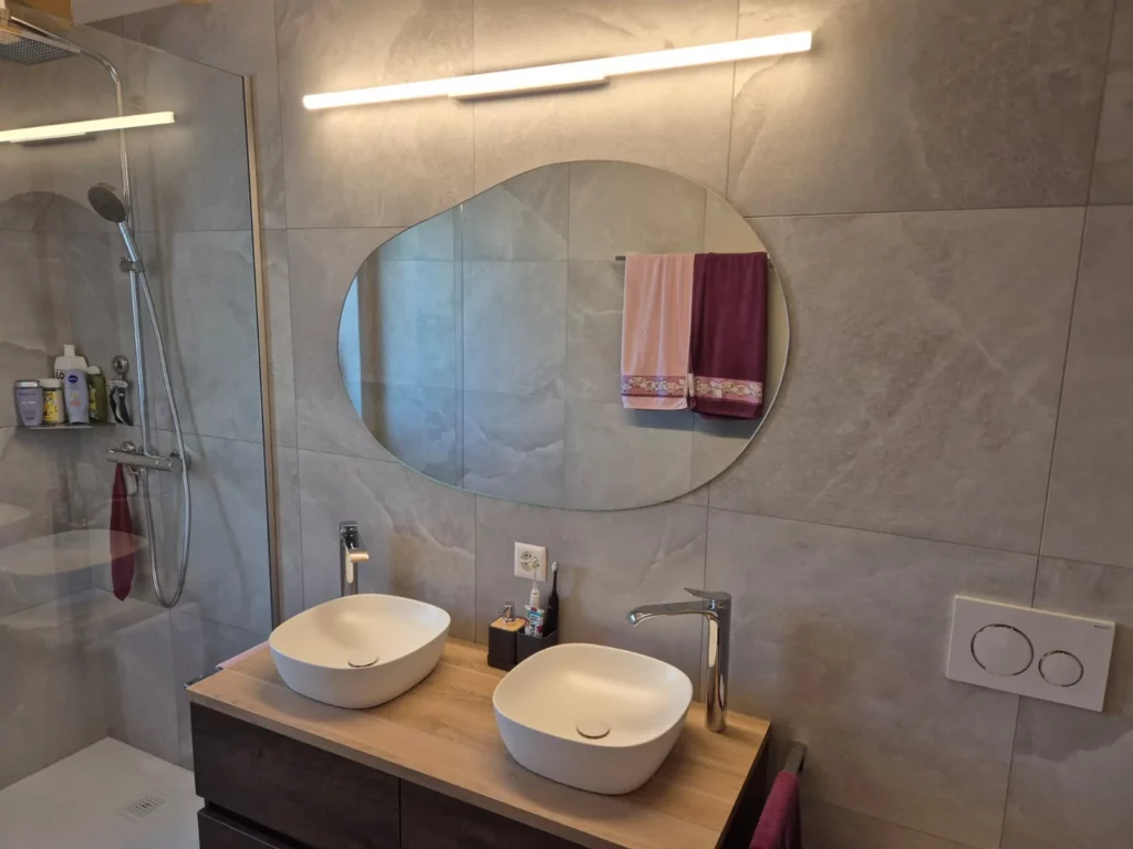 Miroir de forme organique sur mesure installé au-dessus d’un meuble double vasque dans une salle de bain moderne.
